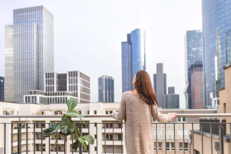 Eine Frau steht auf einer Dachterrasse und schaut in das Frankfurter Bankenviertel